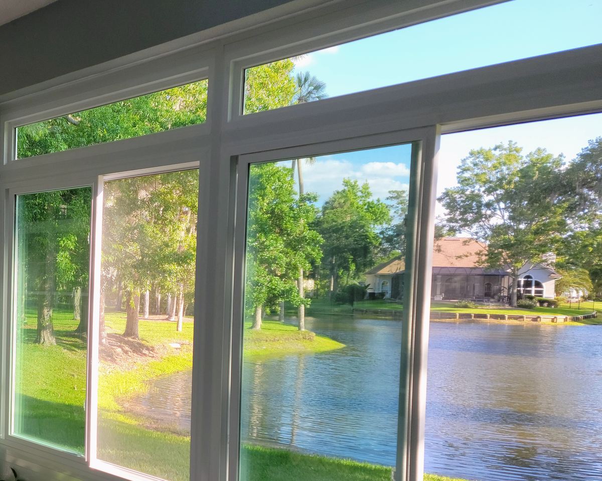 Interior of a sunroom with white-framed windows and transoms overlooking a lawn and pond, completed by Better Home Improvement in Jacksonville, FL